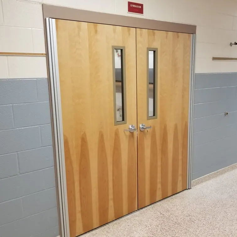 Architectural wood double doors with vision panels and a metal frame at a school gymnasium
