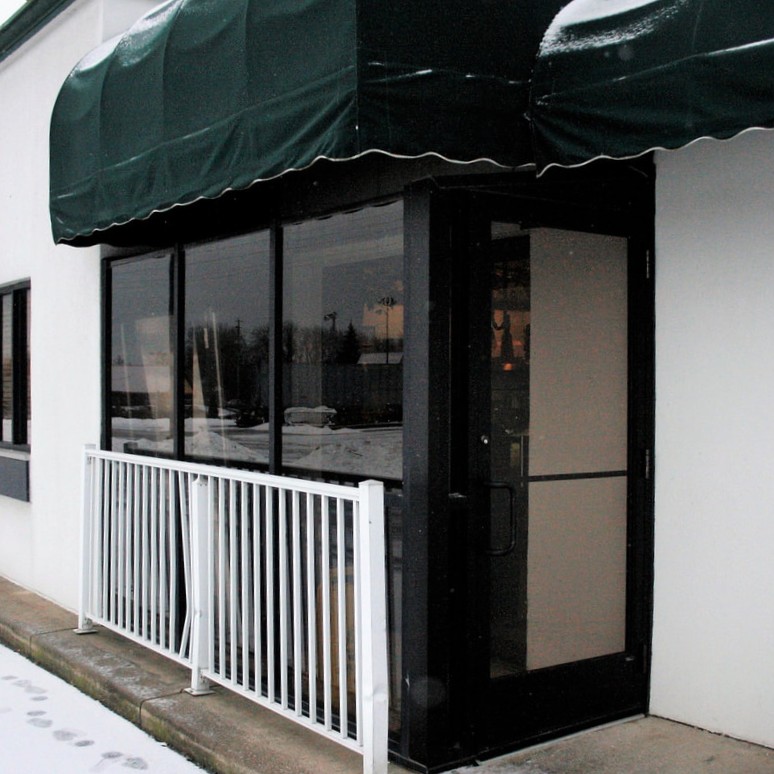 Dark bronze aluminum storefront entrance and windows beneath green awnings
